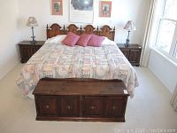 Full view of the king size bed with wooden headboard, nightstands, and blanket with three pink pillows.