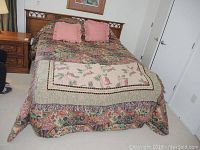 King size wooden bed with floral bed linens and pillows. Bed headboard and frame made of wood with detailed carvings.