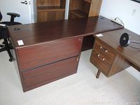 Wide view of the L-shaped wood finish desk with large filing cabinet attached on the left side and smaller filing cabinet on the right, showing keys and desk surface.