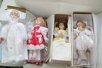 Four porcelain dolls inside boxes and protective plastic packaging, showing dolls' faces and outfits