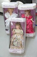 Three boxed porcelain dolls from the Birthstone Collection featuring April Diamond in white, June Pearl in floral cream satin, and July Ruby in pink dress.