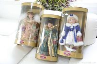 Lot of 3 unopened Collectible Memories porcelain dolls, each in clear plastic and gold-colored cylindrical packaging.