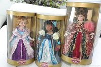 Three Collectible Memories porcelain dolls in original gold-trimmed packaging, shown together in display cases.
