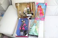 Four boxed Barbie dolls in original packaging arranged on a white surface: George Washington Barbie (pink coat, black pants), Statue of Liberty Barbie (green gown), Hula Hair Barbie (tropical attire), Evening Recital Barbie (with two children dolls).