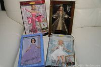 Four Barbie dolls in original boxes shown together on a white surface. Dolls include Elizabeth Taylor as Cleopatra, Marilyn Monroe The 7 Year Itch, Elizabeth Taylor Limited Edition, and Marilyn Monroe Gentlemen Prefer Blondes.