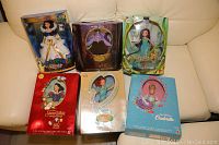 Six boxed Barbie dolls of Disney fairy tale characters arranged on a couch. Dolls include Snow White, Ursula, Tinker Bell, Cinderella, and others.