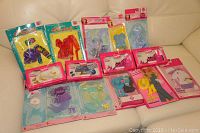 Full view of Barbie clothing and accessories lot displayed on couch, showing multiple unopened packages including dresses, shoes, and other outfits.