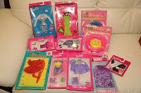 Photo of all items arranged on beige couch showing boxed Barbie clothes and accessories including two feather necklaces and several outfits