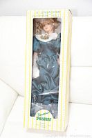 Frontal view of doll in original box showing detailed face, hair and dress.