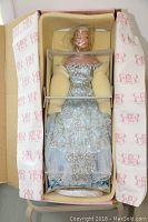 Full doll in original box showing light blue embroidered gown, protective foam padding, and original packaging.