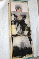 View of the full boxed porcelain doll still in original packaging with styrofoam separators and wrapped components.