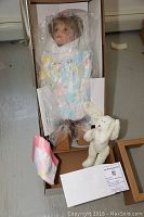 Porcelain doll EVA in original box with plastic protective wrap, white plush bunny, cloth accessory and certificate visible