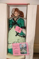 Porcelain doll displayed in original box, fully dressed and secured with plastic ties and foam supports.