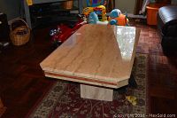 45-degree angle view of beige marble top coffee table on a patterned rug with some toys around.