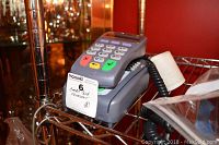 Front view of VeriFone Omni 5100 credit card processor on its base, showing keypad, display, and attached coiled phone cable.