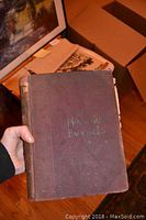 Front cover of the antique book showing the title 'The Household Encyclopedia' with worn purple fabric cover and worn edges.