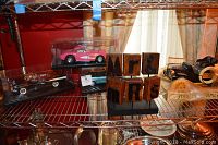 Shelf display showing three model cars in plastic boxes, including a pink Corvette, blue Ford Mustang, and black Chevrolet Bel Air convertible.