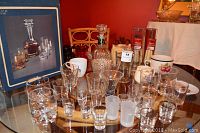 Photo showing the whiskey set including crystal decanter, assorted shot glasses, and tumblers arranged on a table with original box behind.