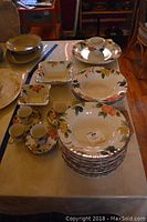 Overview of various Mikasa Fruit Panorama dishware arranged on table including large and soup bowls, square bowls, plates, and demitasse cups with saucers.