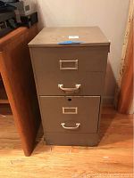 Front view of the filing cabinet showing two drawers with pull handles and label holders, stains visible on top surface.