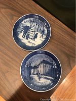 Two blue and white round Hans Christian Andersen Christmas plates marked 1970 and 1973 by Desiree Old Copenhagen Blue, each plate has winter and architectural illustrations.