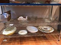 Metal shelving with multiple plates and bowls including clear glass items, decorative plates, and ceramic dishes.