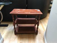 Front view of wooden end table showing rectangular top, two shelves, and turned legs on hardwood floor.