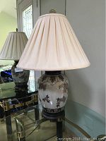 Full view of the table lamp showing the ceramic floral base, beige pleated shade, and wooden stand.