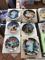 Six Disney collectible plates displayed on their boxes showing scenes from various movies including Cinderella, Pinocchio, Beauty and the Beast, The Little Mermaid, and Pocahontas.