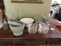 Whole lot displayed on wooden table with decorative wall art behind, showing decanter, glasses, mortar and pestle, salt cellars, beer glasses, decorative bottle.