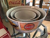 Three ceramic nesting bowls branded with Coca-Cola graphics with vintage style imagery.