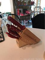 Overview of wooden knife block with seven knives, scissors, and sharpener all with red handles on a white surface