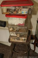 Stack of four plastic bins filled with assorted rocks, minerals, geodes and small containers on metal stool.