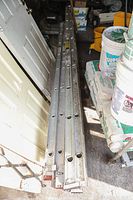 Overall view of the three aluminum ladders stacked parallel in a storage area, showing length and condition with some dirt and stains.