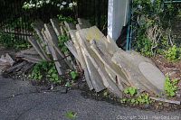 Wide view of two stacks of large flat stones leaning against a gate and fence with foliage