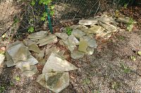 Multiple stacks of flat stones placed outdoors on soil and gravel near a fence.
