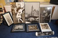 Overall view of seven framed black and white wall art and posters arranged on floor showing variety of city themes and vintage imagery