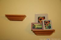 Two lighter stained wooden wall shelves mounted on a wall, one holding three framed pictures.