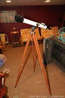 Full view of Edu Science white telescope mounted on wooden tripod in a room with brown carpet and furniture.