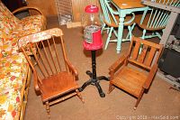 Photo of two child wooden rockers and a vintage red gumball machine on black pedestal stand.