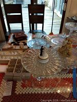 Multiple glass cake plates and trivets on a table including a bride and groom figurine cake topper.