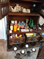 Photo of various candles including pillar candles in red, orange, blue, white, cream, and brown on a wooden shelf along with spherical candles and some glass and ceramic holders.