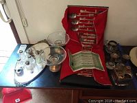 Full view of the lot with Shelton utensils in red fabric case, glass candy dishes, salt and pepper shakers, and Jack Daniels liquor sleeve with shot glass on table.