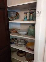 Shelf of assorted pottery items including large dishes, two candle holders, and a ceramic jar with lid.