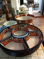 Photo of a large black lazy susan with six segmented compartments decorated with Asian style floral and geometric motifs in red, orange, blue, and white.