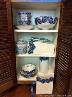 Full view of shelving unit with blue and white ceramic bowls, vases, pot and plates arranged inside showcasing the blue leaf pattern decoration.