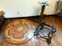 Photo of the 38.5 inch round mosaic tile tabletop with bright floral pattern and two wrought iron bases with scroll design and a standing wrought iron leg assembly component.