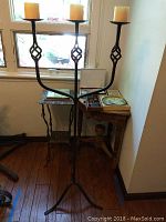 Wrought iron floor candelabra with three candles positioned near tables and window, showing decorative detail and structure