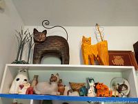 Overview of shelf with a variety of cat decor pieces including metal, ceramic, wooden items clustered together
