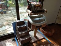 Photo showing the plastic cat carrier with attached carpeted steps and decorative cat pillows on top in front of a glass door.